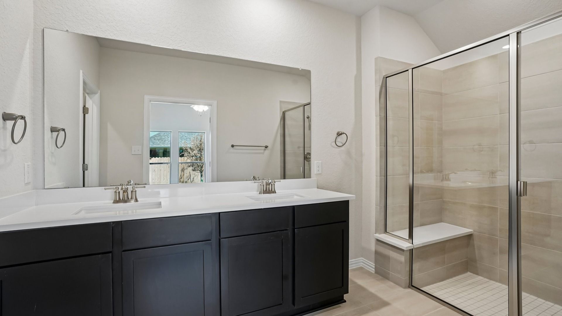 Owner's bath with ceramic tile shower, built-in seat, and double vanity featuring espresso cabinets and white countertops.