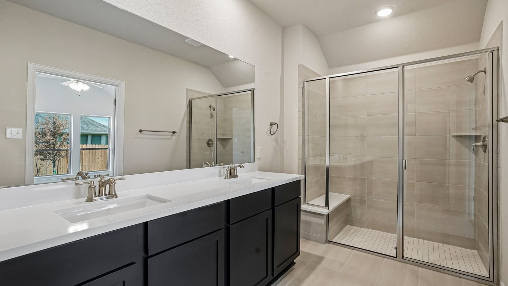 Owner's bath with ceramic tile shower, built-in seat, and double vanity featuring espresso cabinets and white countertops.
