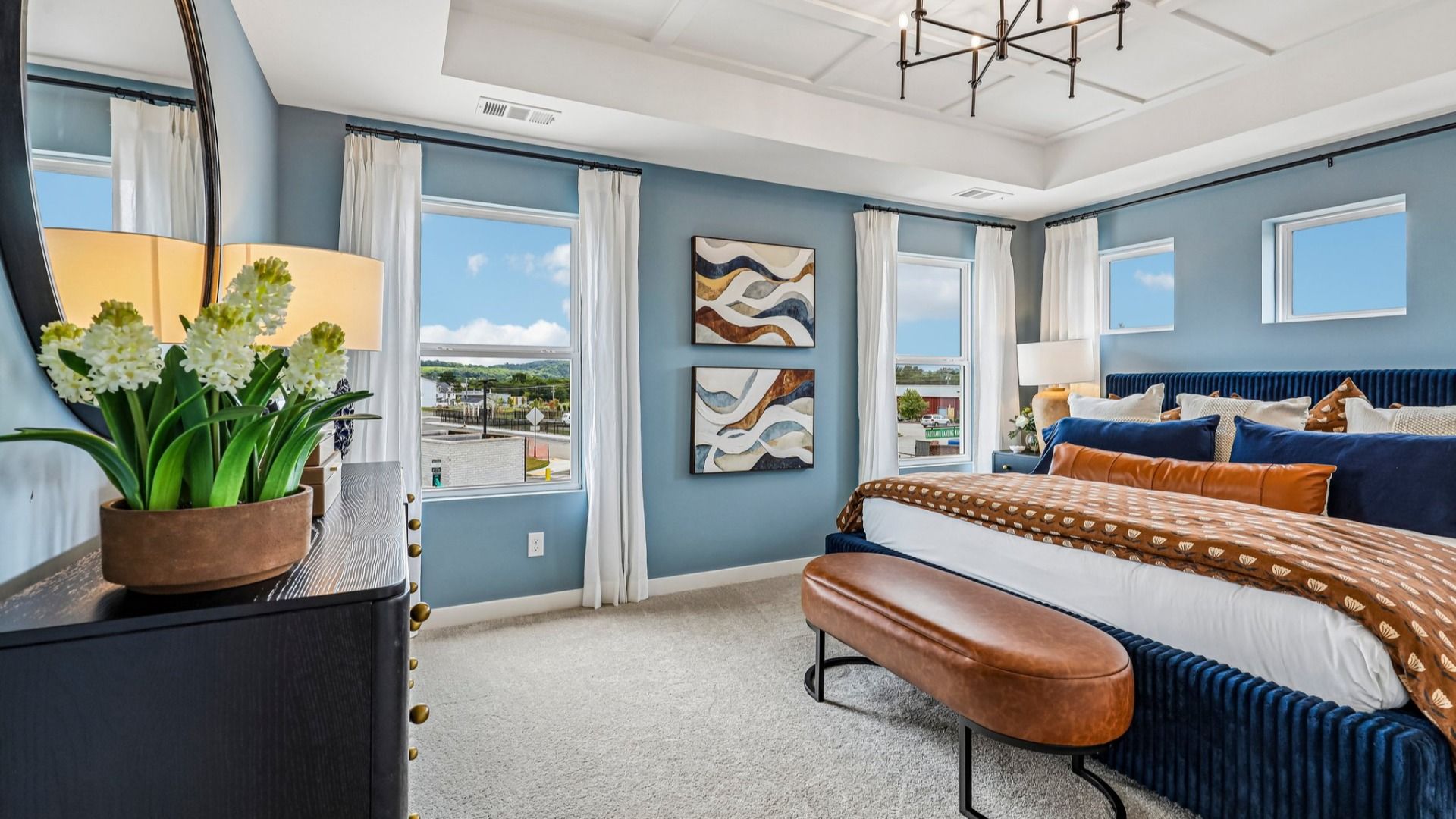 Primary suite with tray ceiling, windows, and carpet