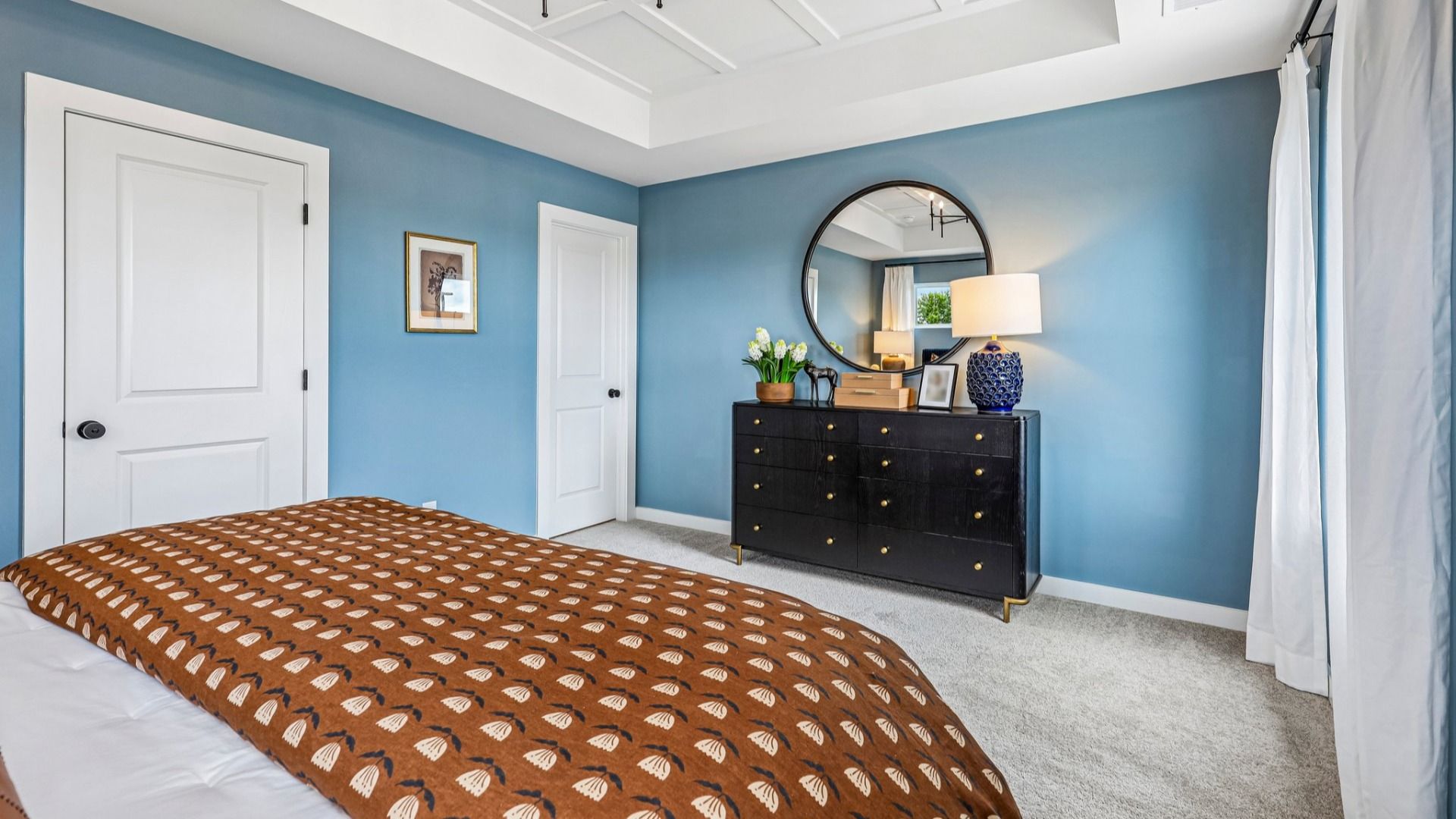 Primary suite with tray ceiling, windows, and carpet