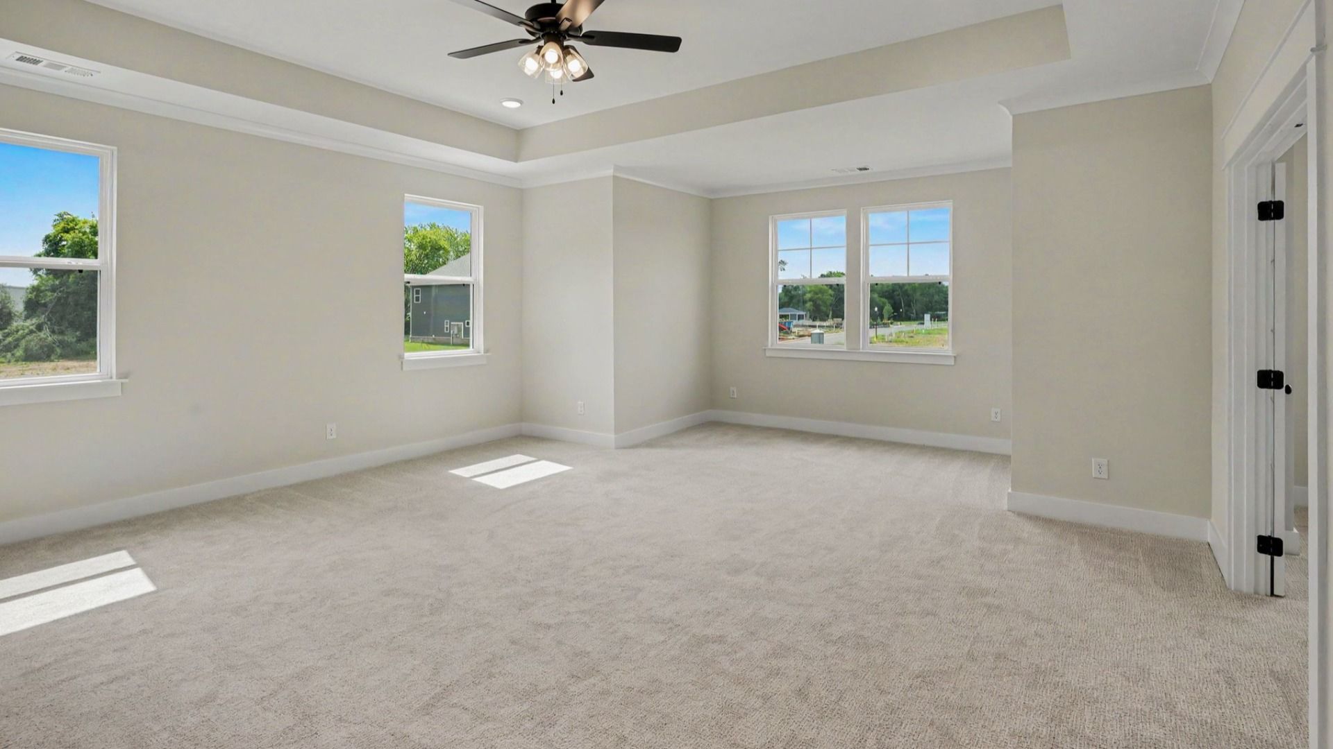 Primary suite with tray ceiling, ceiling fan, and carpet