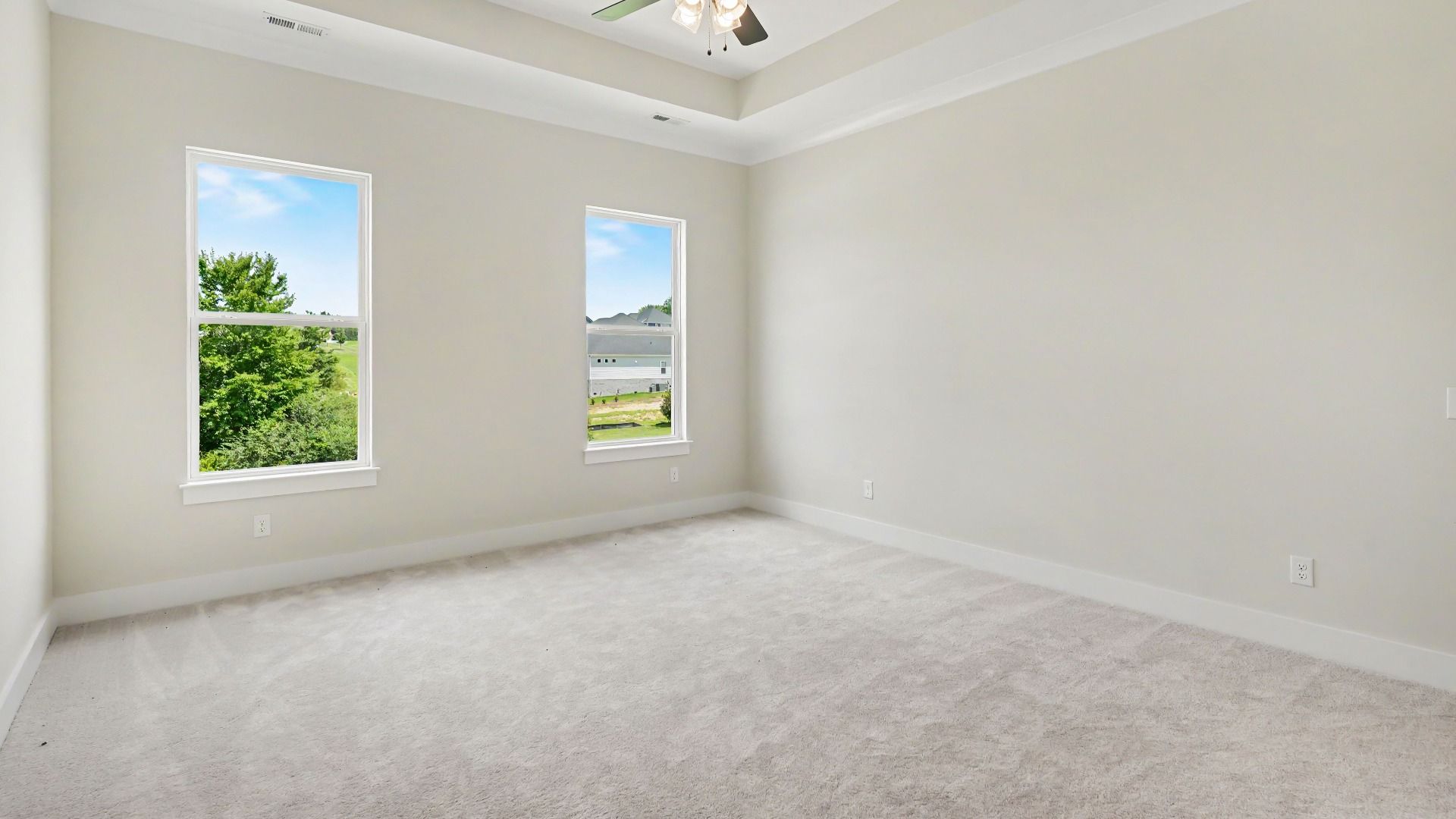 Primary suite with tray ceiling, ceiling fan, and carpet