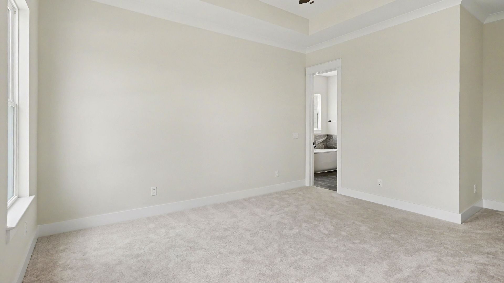 Primary suite with tray ceiling, ceiling fan, and carpet