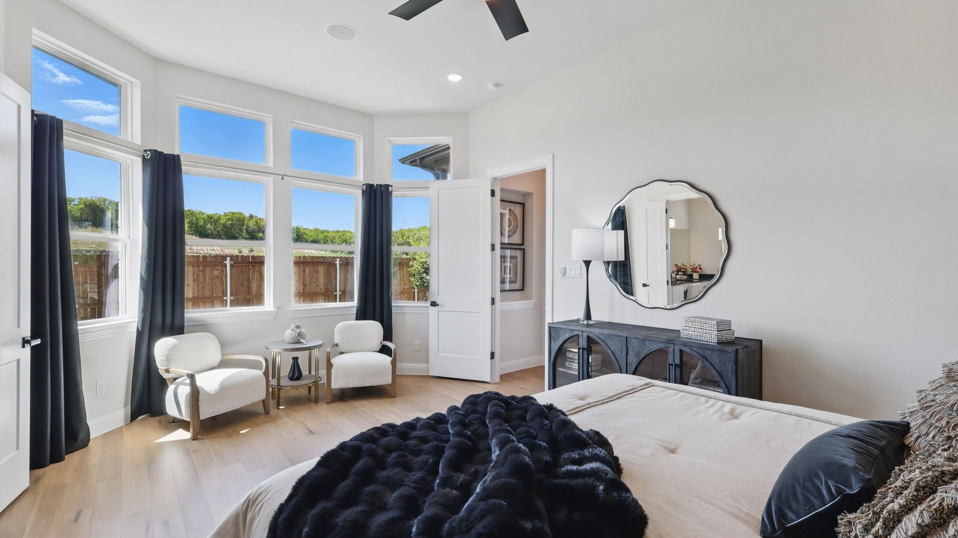 Bright primary suite featuring large windows, a sitting area, and elegant designer finishes.