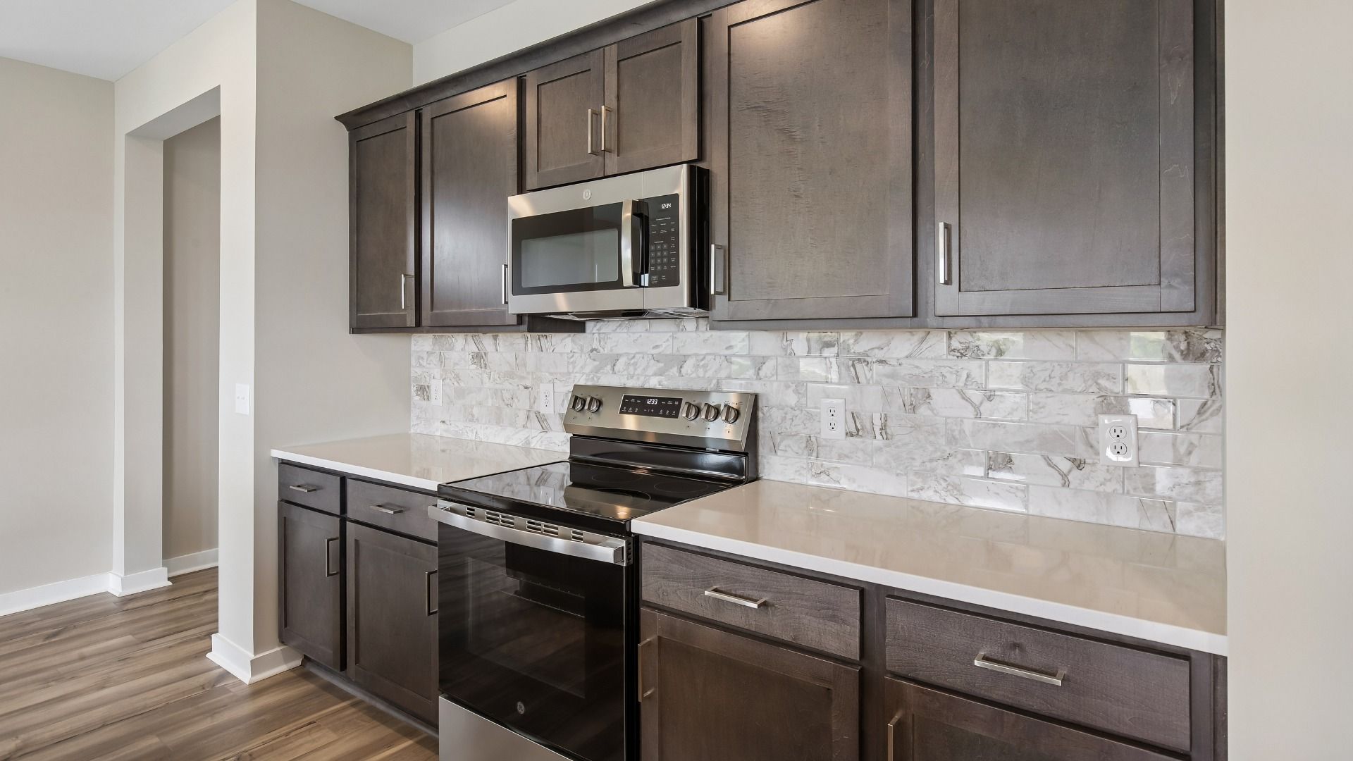 Kitchen with dark cabinetry, quartz countertops, stainless steel appliances, and tile backsplash