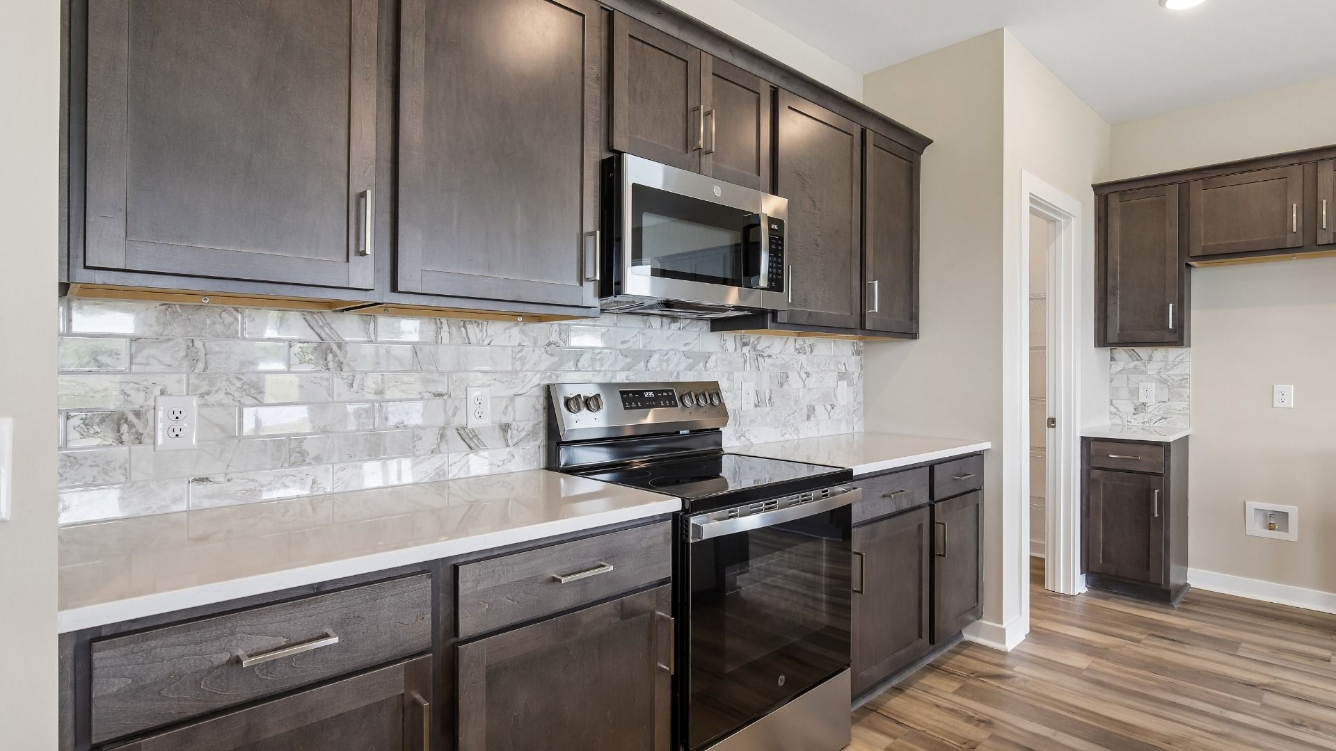 Kitchen with dark cabinetry, quartz countertops, stainless steel appliances, and tile backsplash