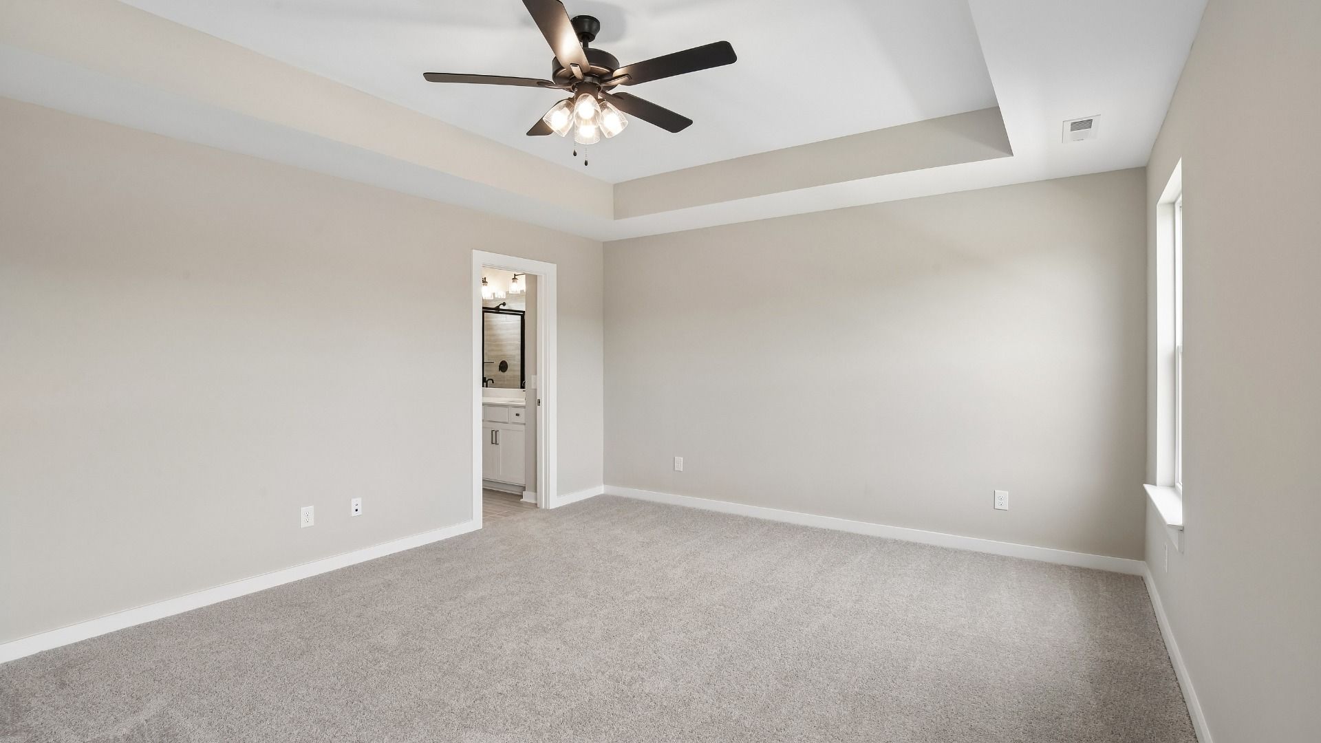 Bedroom with tray ceiling, windows, and en-suite primary bathroom