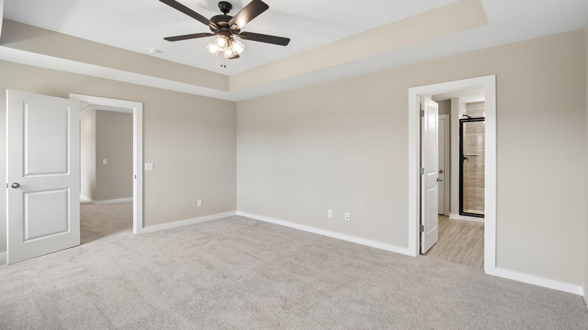 Bedroom with tray ceiling, windows, and en-suite primary bathroom