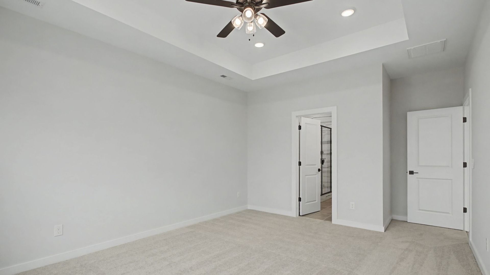 Primary bedroom with tray ceiling and ceiling fan, and door to en-suite bathroom
