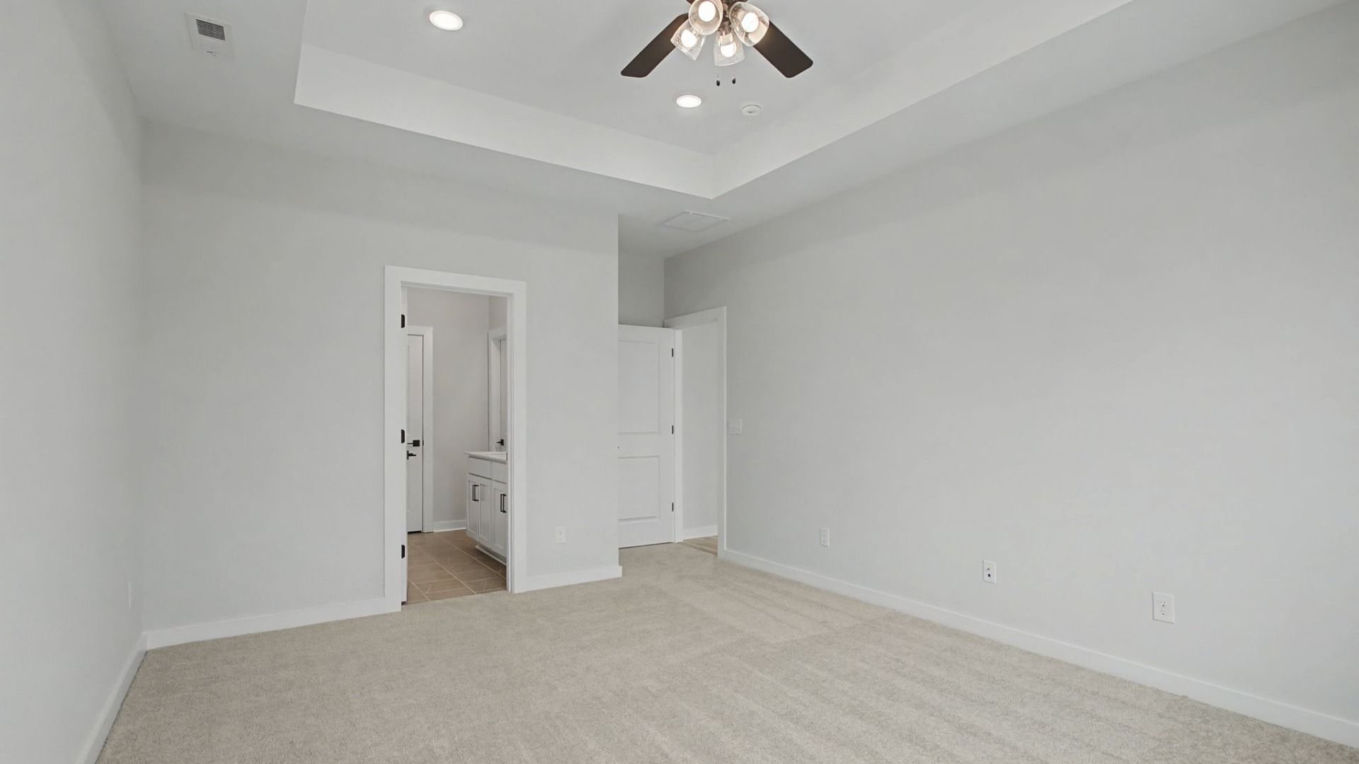 Primary bedroom with tray ceiling and ceiling fan, and door to en-suite bathroom