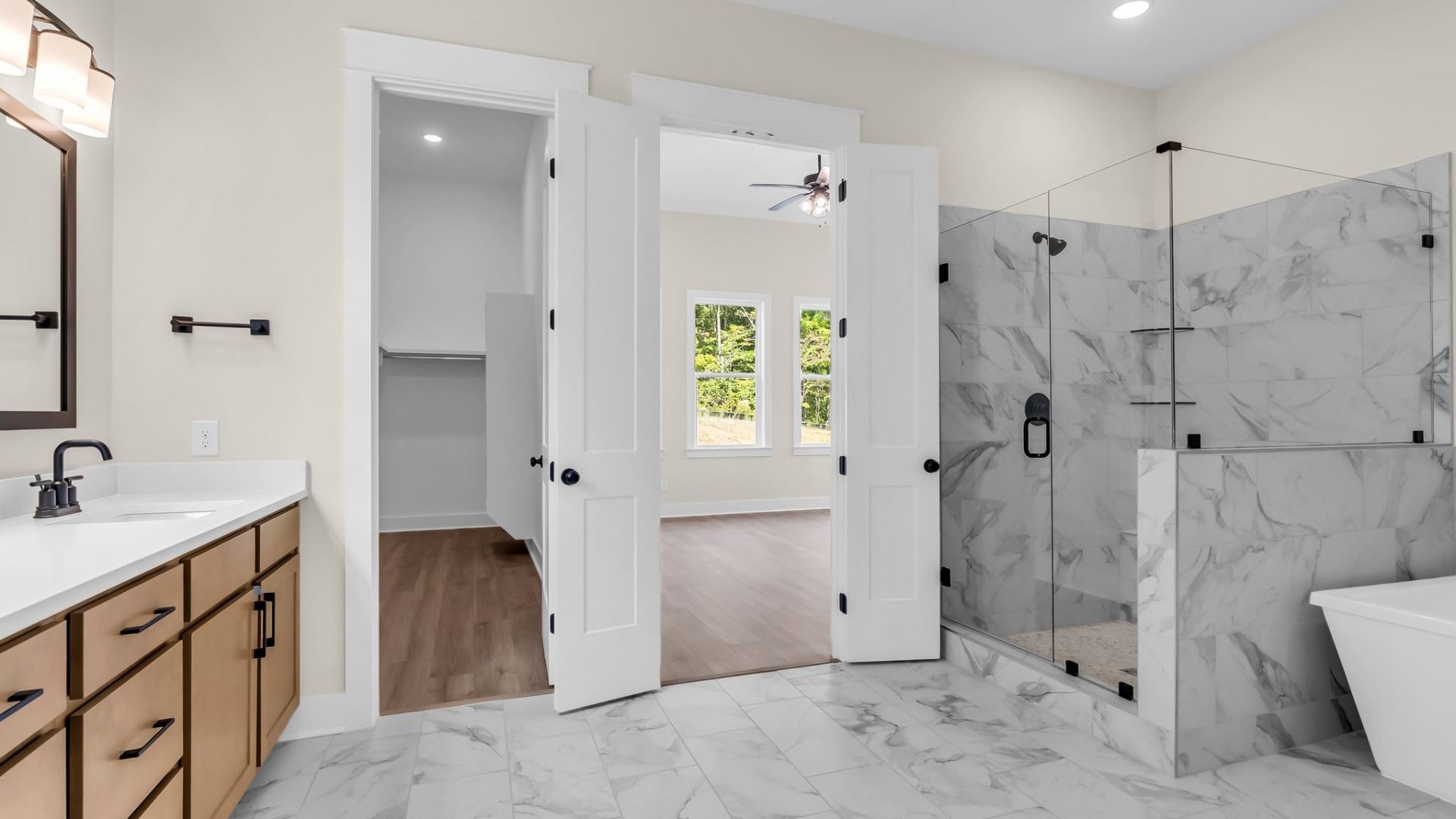 Primary suite bathroom with gorgeous tile, frameless shower, freestanding tub, and walk in closet`