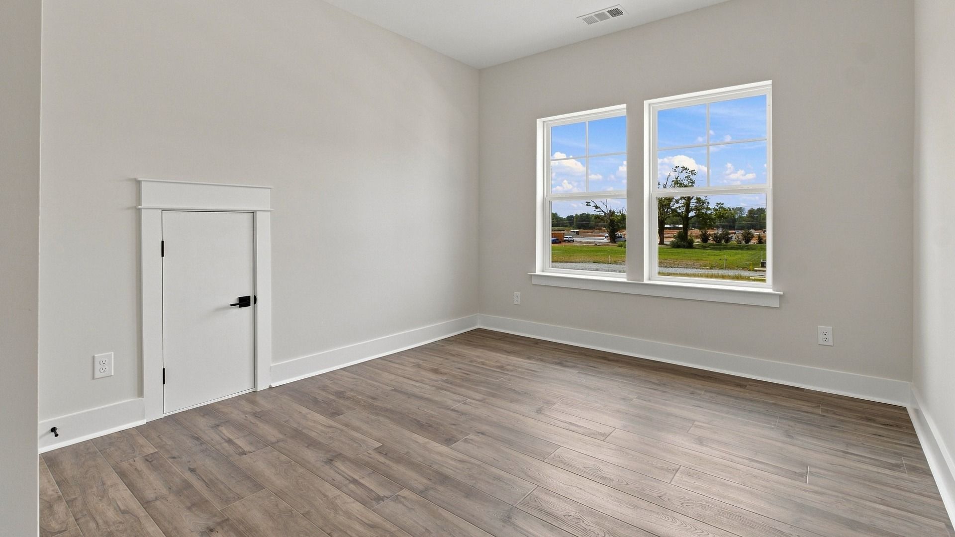 Upstairs bedroom with elevated wood flooring and two windows.