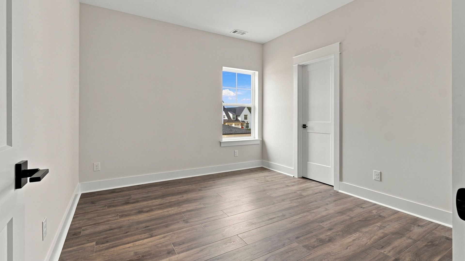 Spacious bedroom with hardwood flooring with one window and closet space.