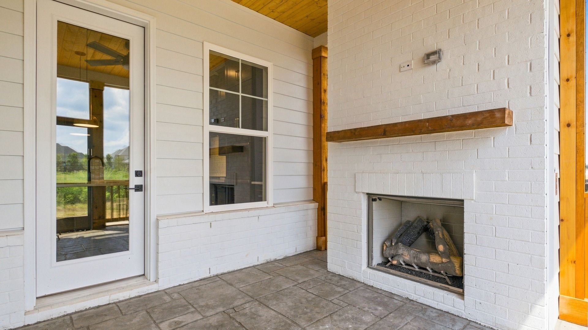 View of backyard door from porch screen door showcasing an elevated fireplace for outdoor living.