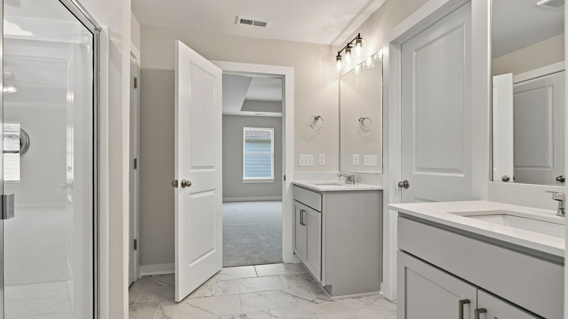 Primary bathroom entry way door next to convenient separated dual vanities