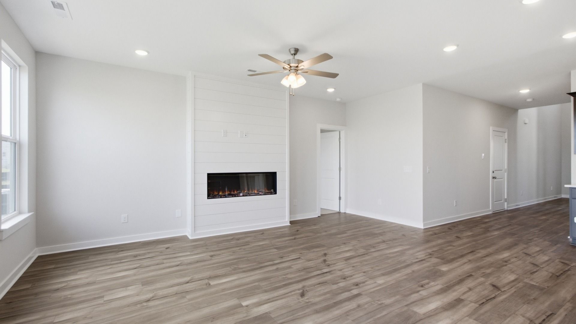 Spacious living area with elevated features such as hardwood floors, electric fireplace, and ceiling fan