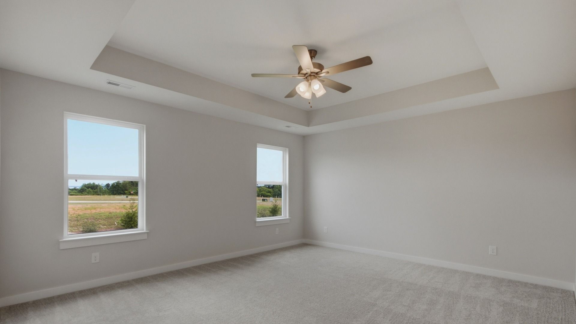 Elevated primary bedroom with tray ceilings and fan