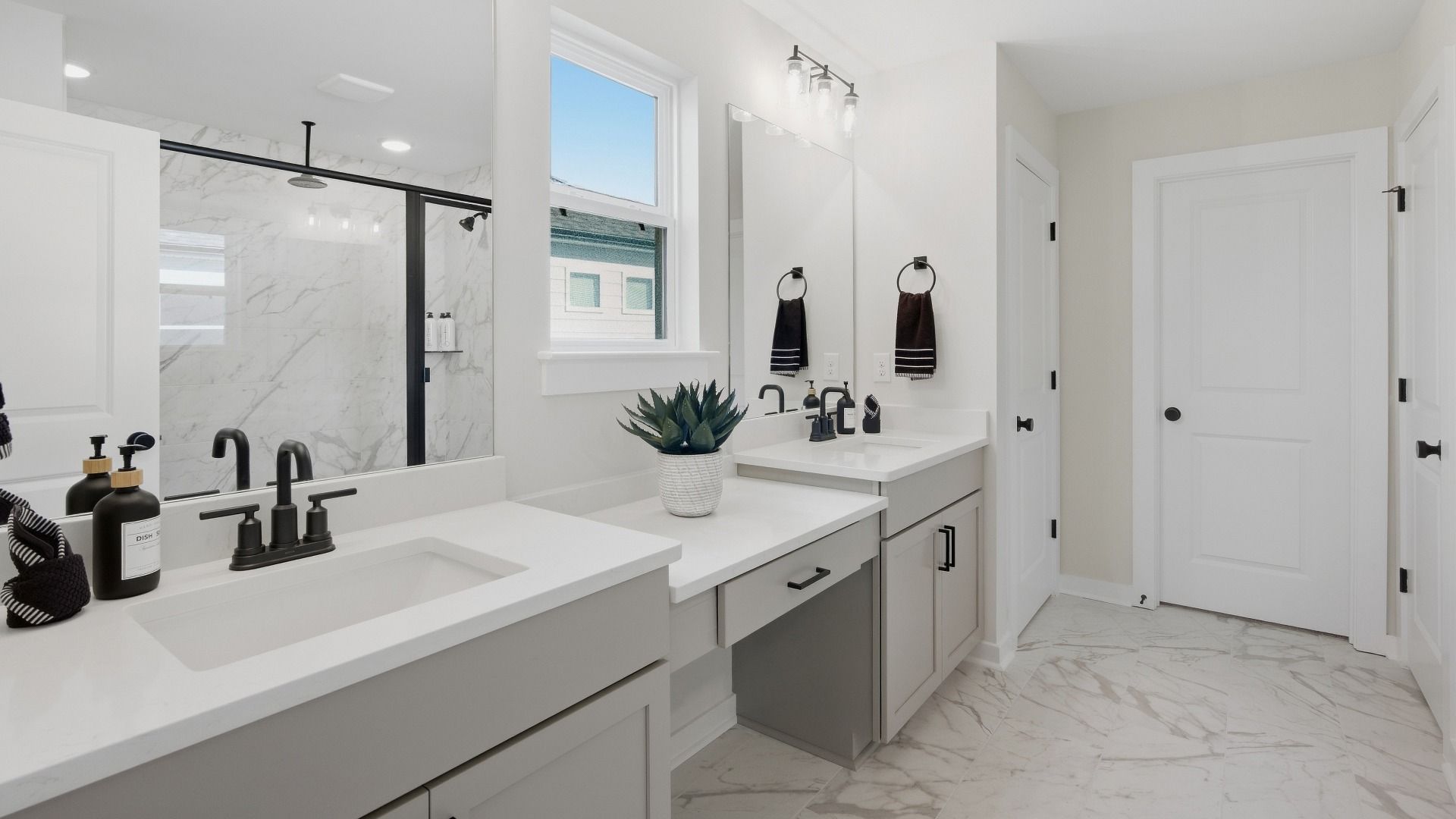 Connected primary bathroom with dual vanities paired with sizeable mirror