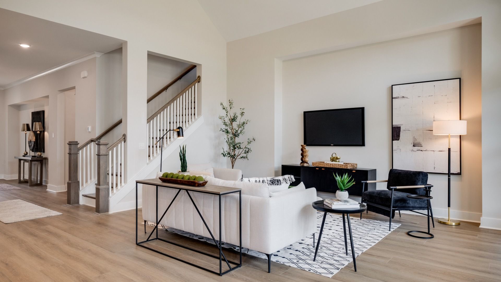 Large living room area with vaulted ceiling next to staircase and kitchen