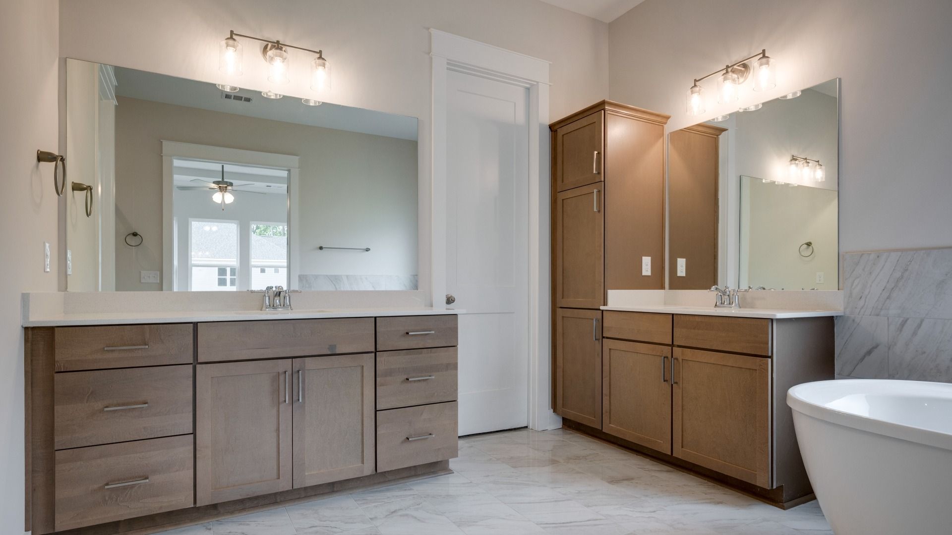 Large tiled primary bathroom with multiple vanities, glass shower enclosure, and freestanding tub