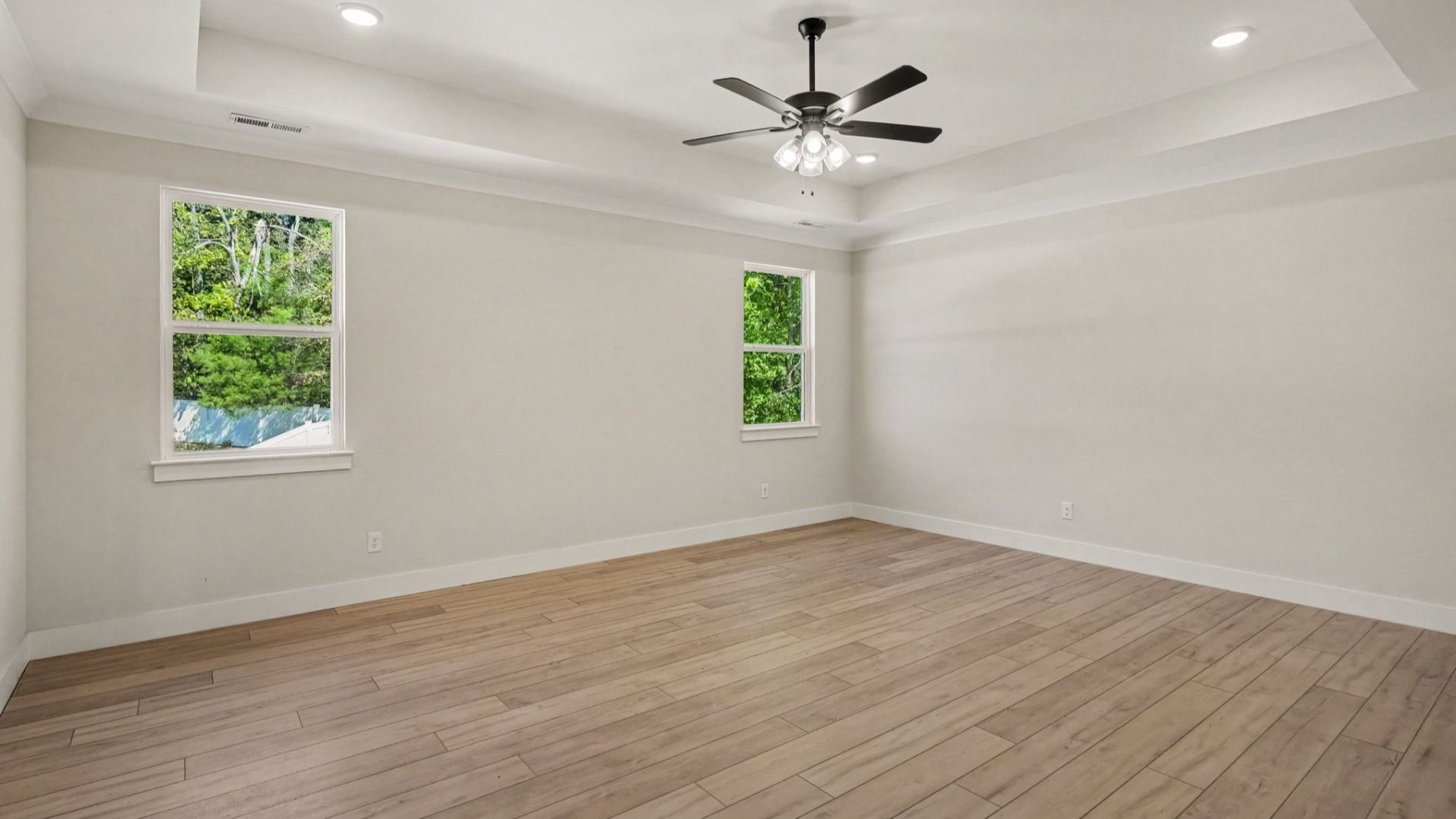 Primary bedroom with tray ceilings and fan