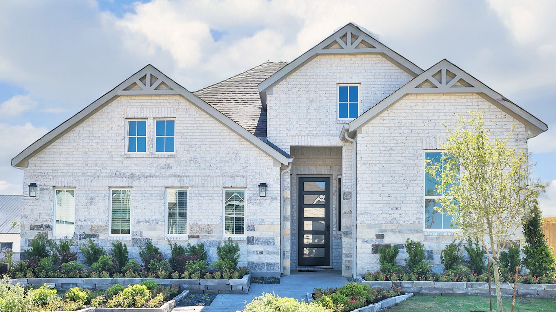 Exquisite white brick facade with gabled roof and geometric door, surrounded by lush landscaping in Southern Pointe.