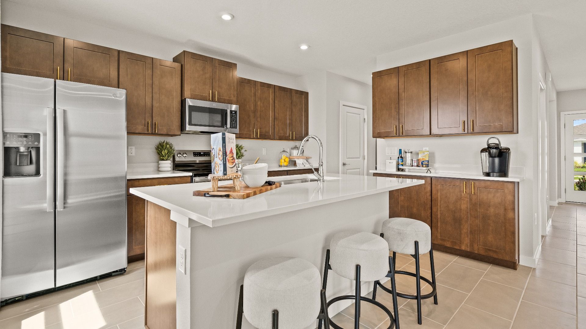 The Highbourne model’s kitchen features warm wood cabinetry, a large island with bar seating, and sleek stainless appliances.