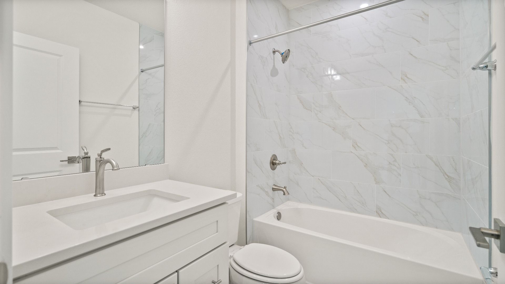 Modern secondary bathroom with white vanity, chrome fixtures, and marble-style tile accents