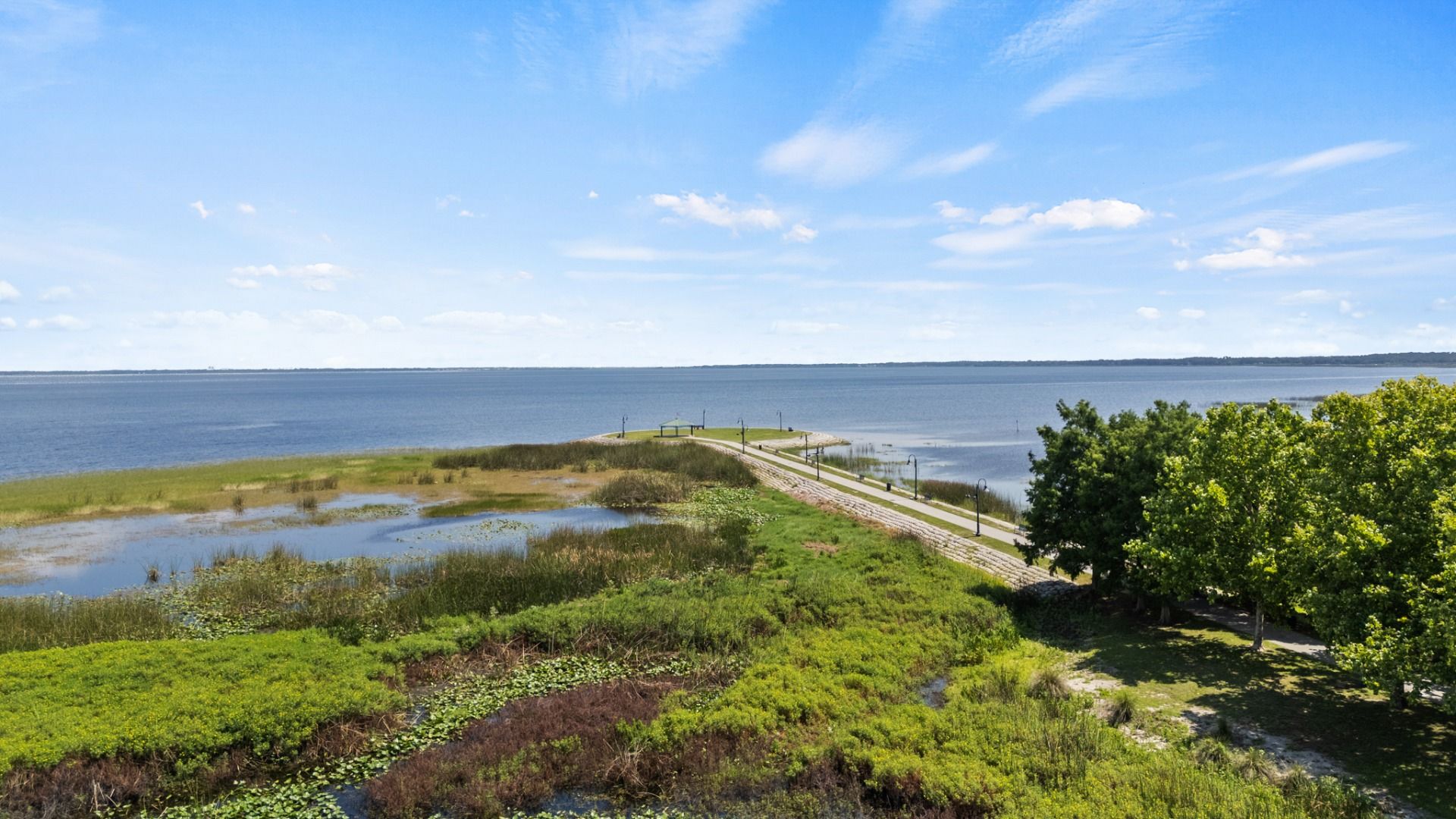 Scenic view of Lake Tohopekaliga from St. Cloud, FL featuring lush greenery and a walking path near Cyrene at Harmony.