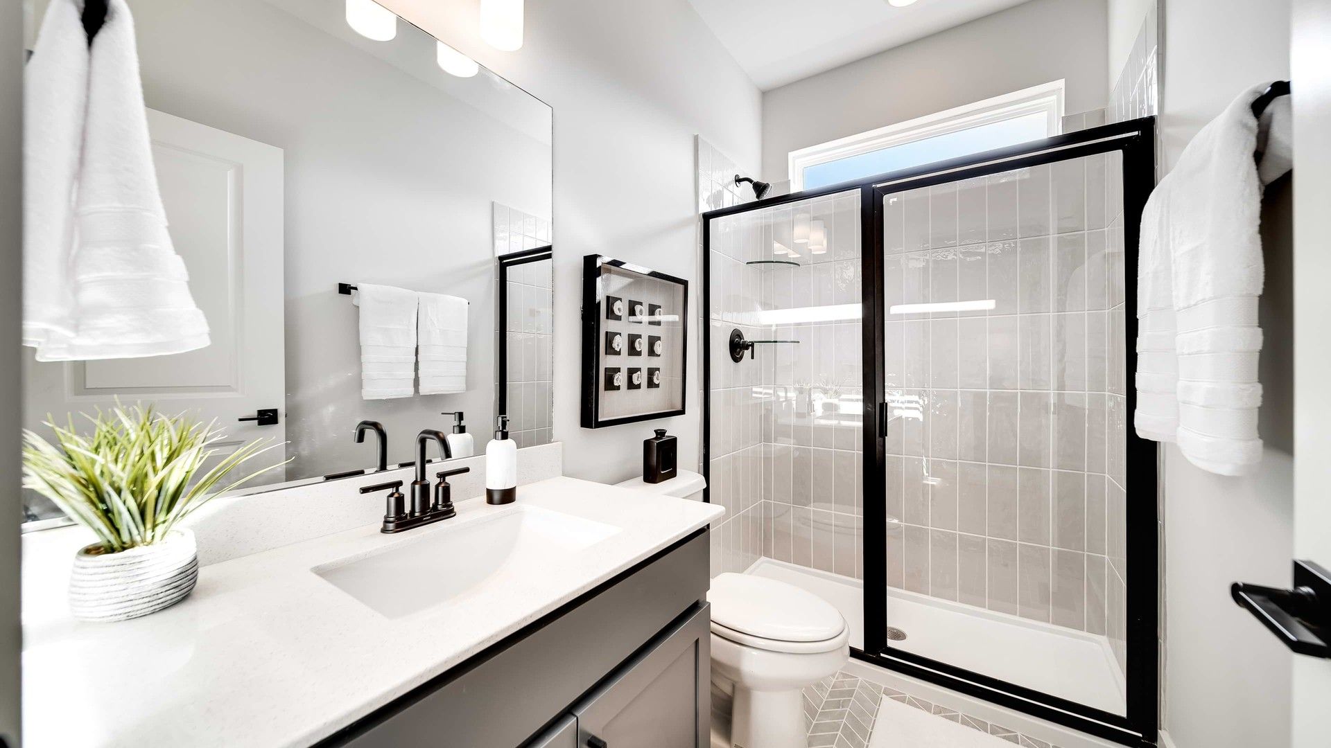 Experience sleek black fixtures and refined geometric tiles in Richvale Estates' elegant bathroom design.