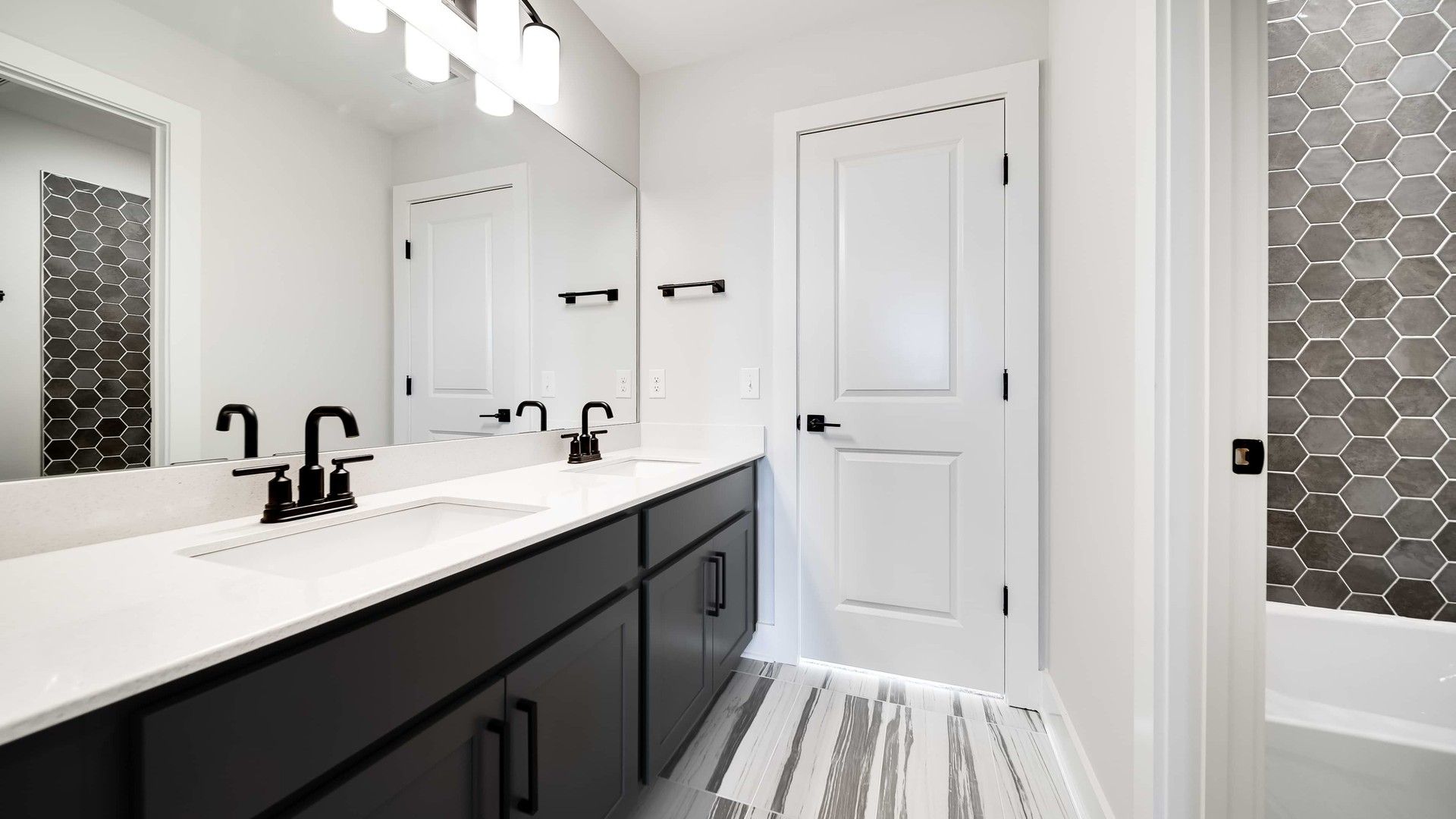 Elegant bathroom in Richvale Estates featuring hexagonal tiles, black fixtures, and dual sinks.