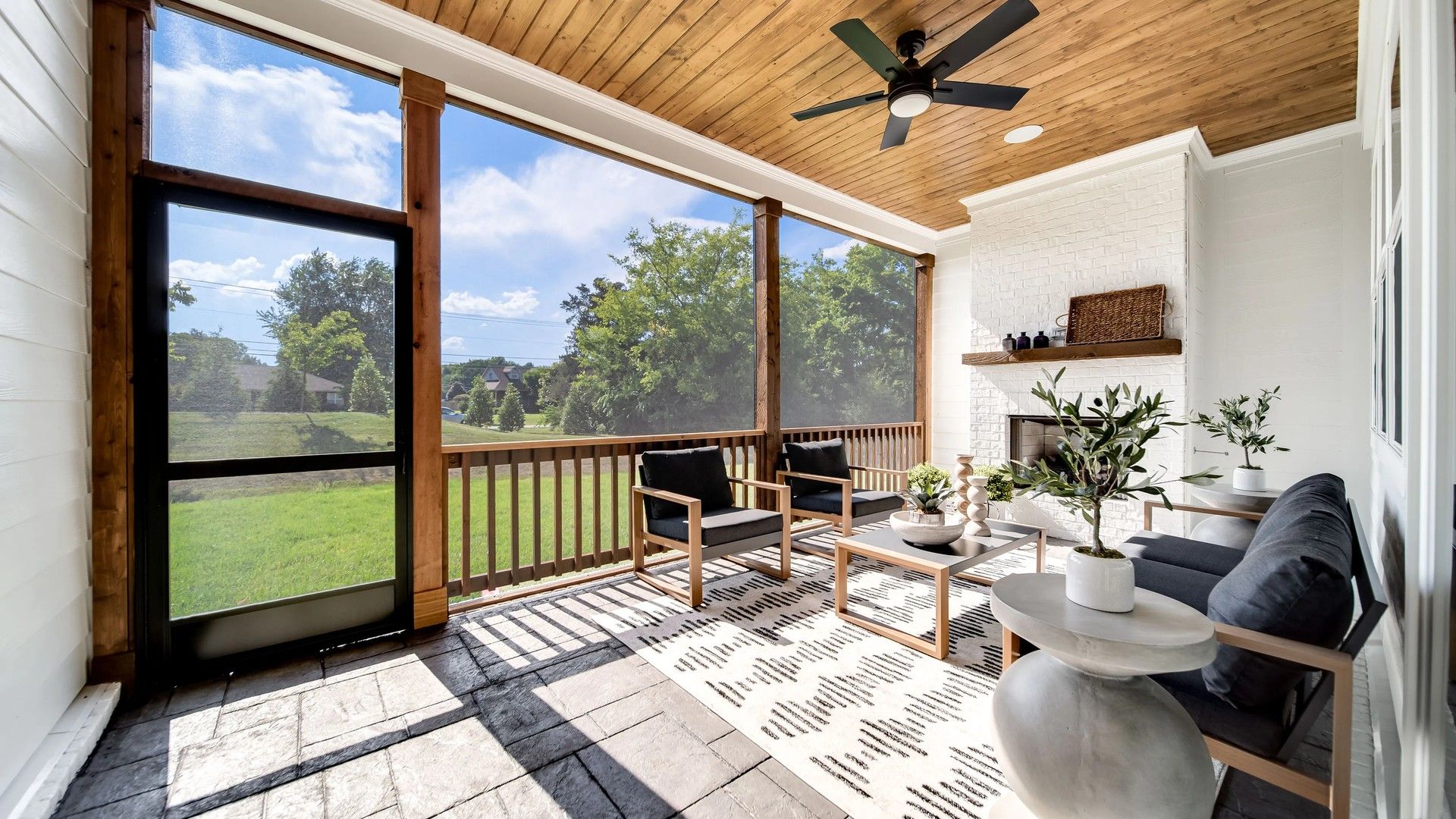 Luxurious screened porch with rich wood ceiling, stone flooring, and chic fireplace in Shelton Square, TN.