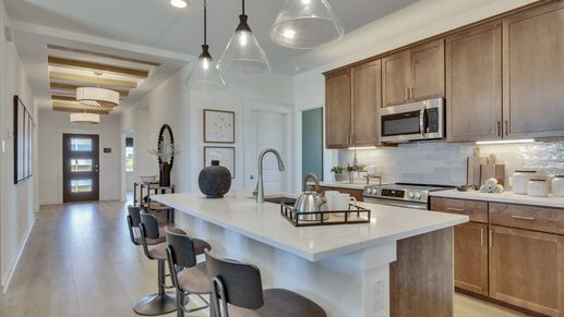 Sleek wooden cabinetry, modern appliances, and custom lighting highlight this luxurious Hunters Glen kitchen.