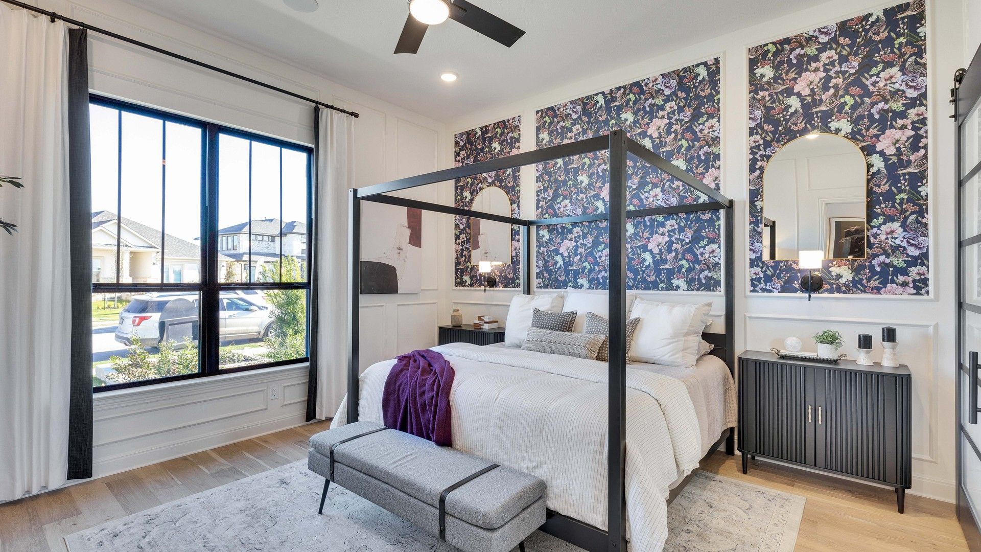 Sophisticated bedroom with floral accent wall, sleek hardwood floors, and a chic canopy bed in Flora community.