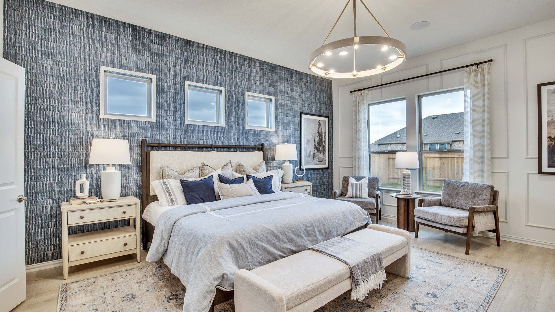 Elegantly designed bedroom features a textured accent wall, modern chandelier, and expansive windows. Opal Ranch.