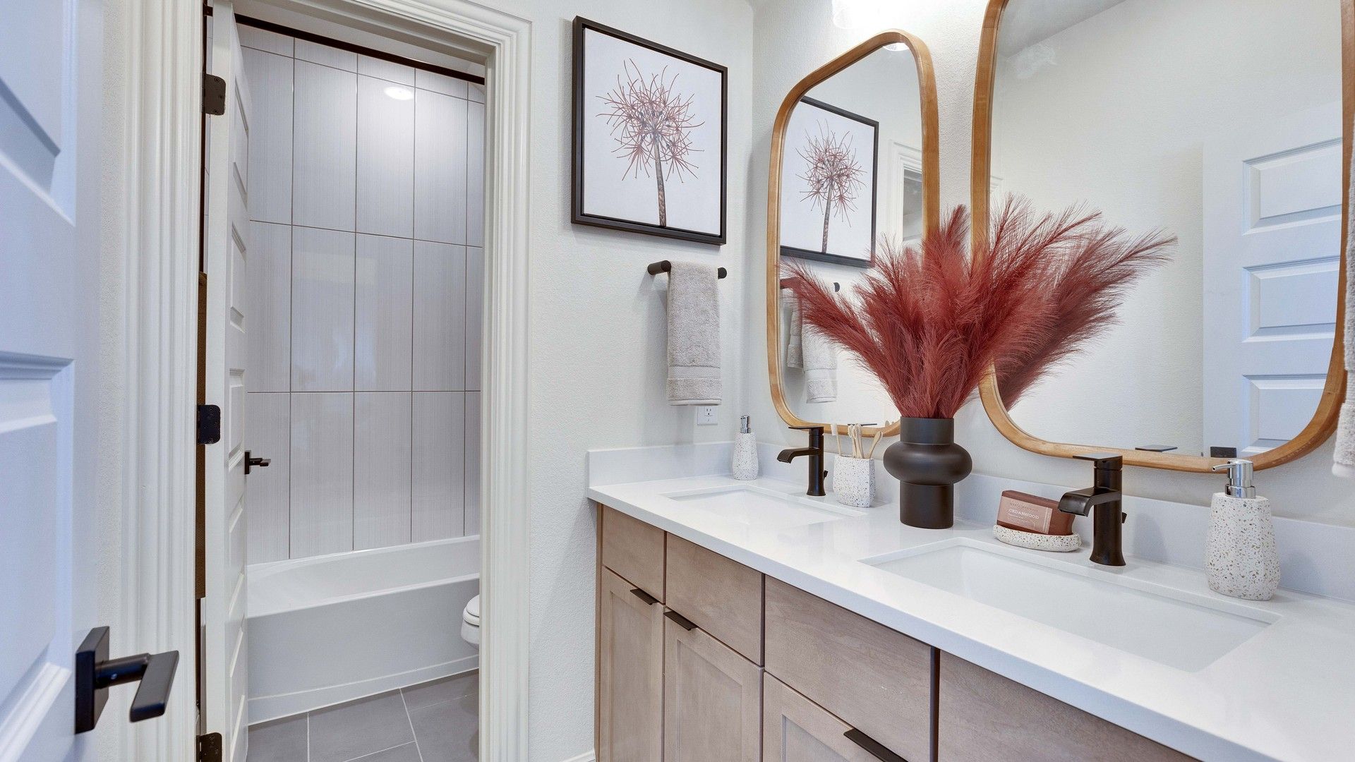 Luxurious twin vanities feature chic natural wood mirrors and sleek fixtures in Flora community.