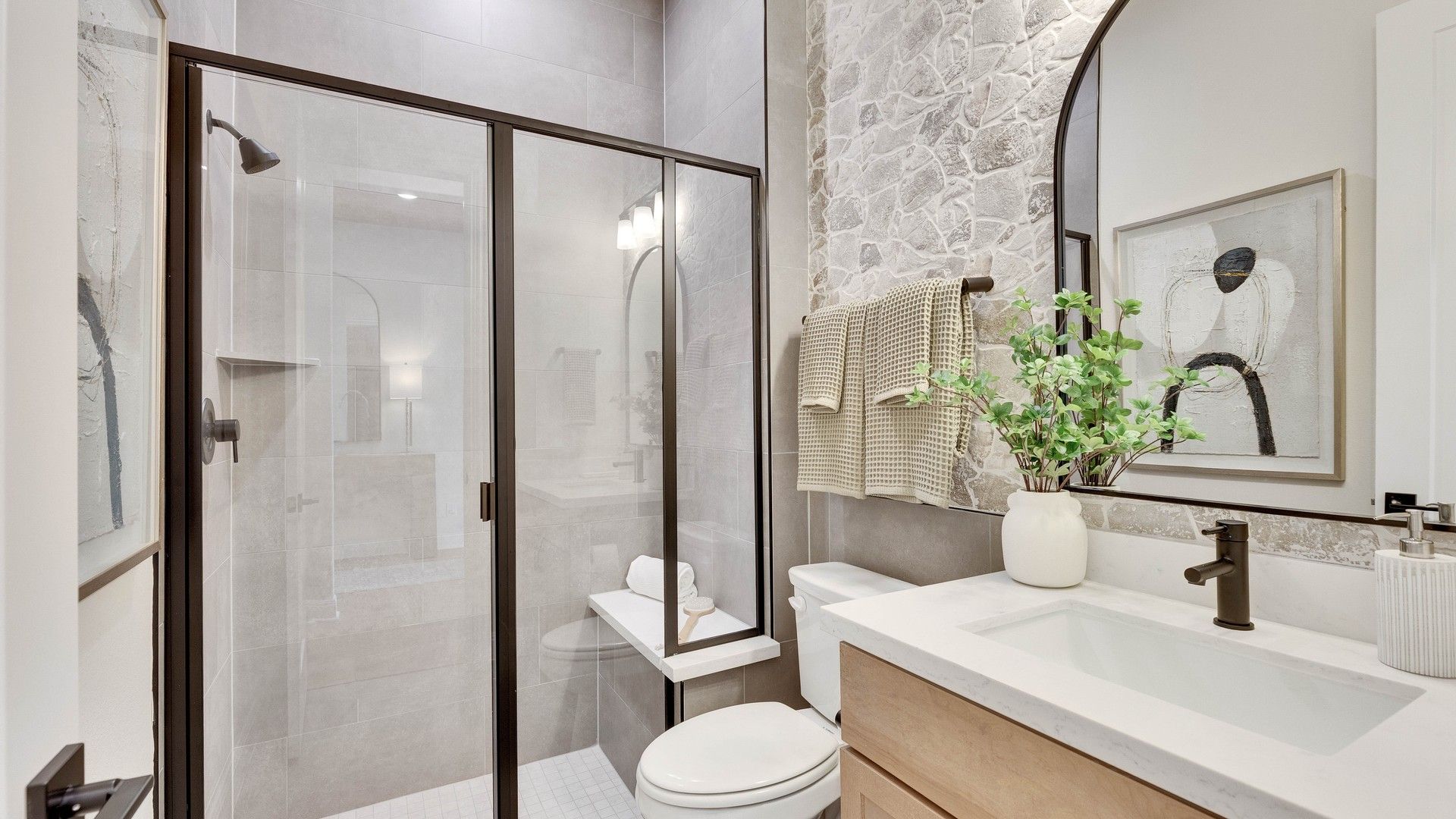 Experience elegance with a glass shower, stone accent wall, and arched mirror in Lakeside Meadows.