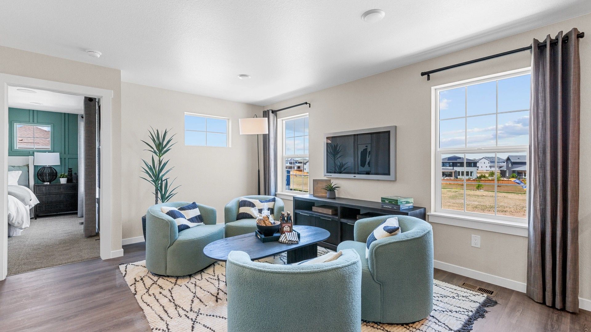Luxurious living space features plush teal seating, expansive windows, and premium wood floors in Timnath Lakes.
