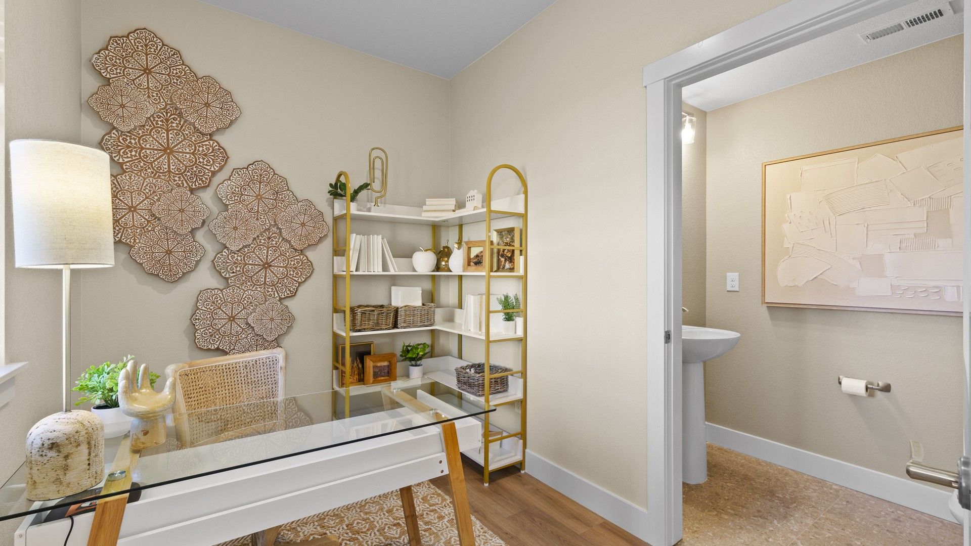 Explore this chic Dillon Pointe office featuring a glass desk, gold shelving, and intricate wall art.