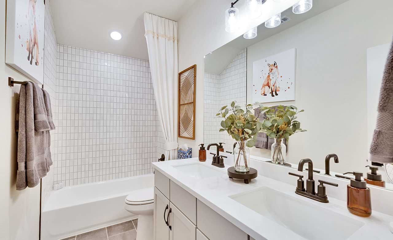 Dual-sink vanity with bronze fixtures and white tiles exude luxury at Retreat at San Gabriel.