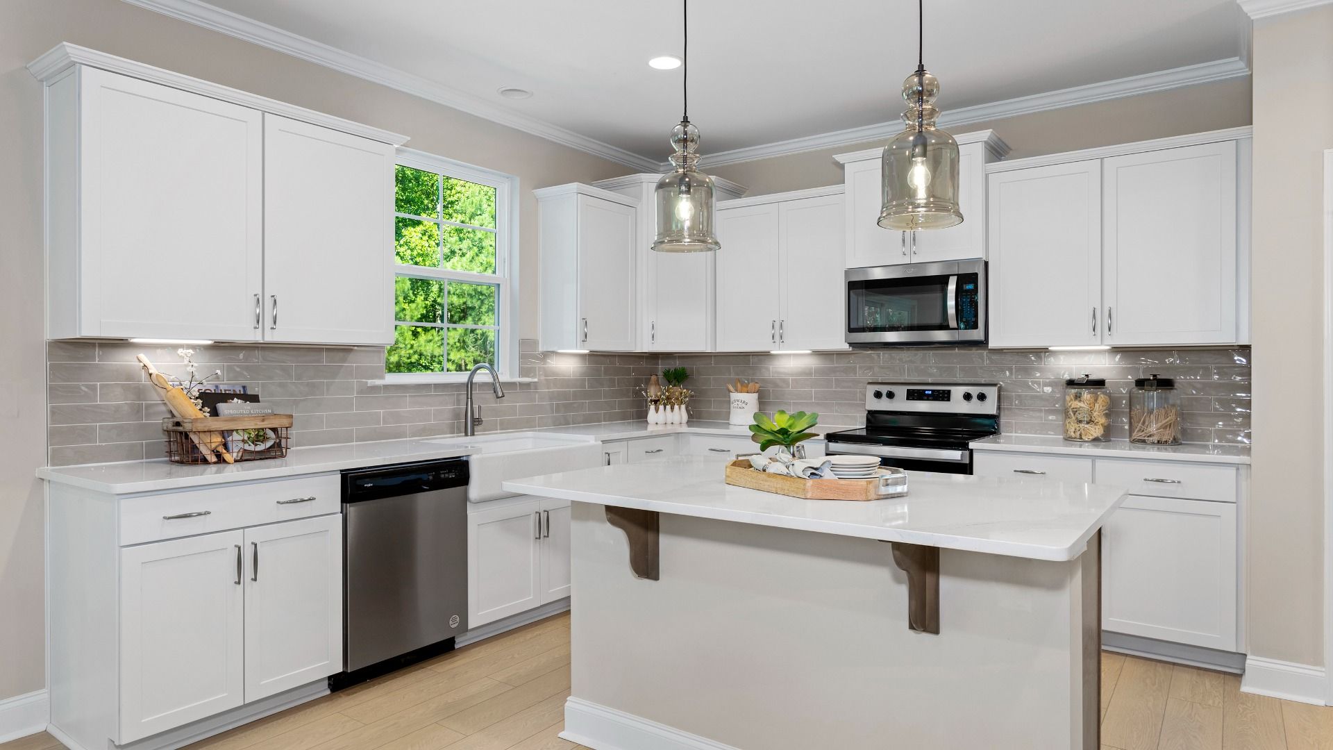 Kitchen featuring island, white cabinetry, stainless steel appliances, light countertops, tile backslash, and pendant lights.