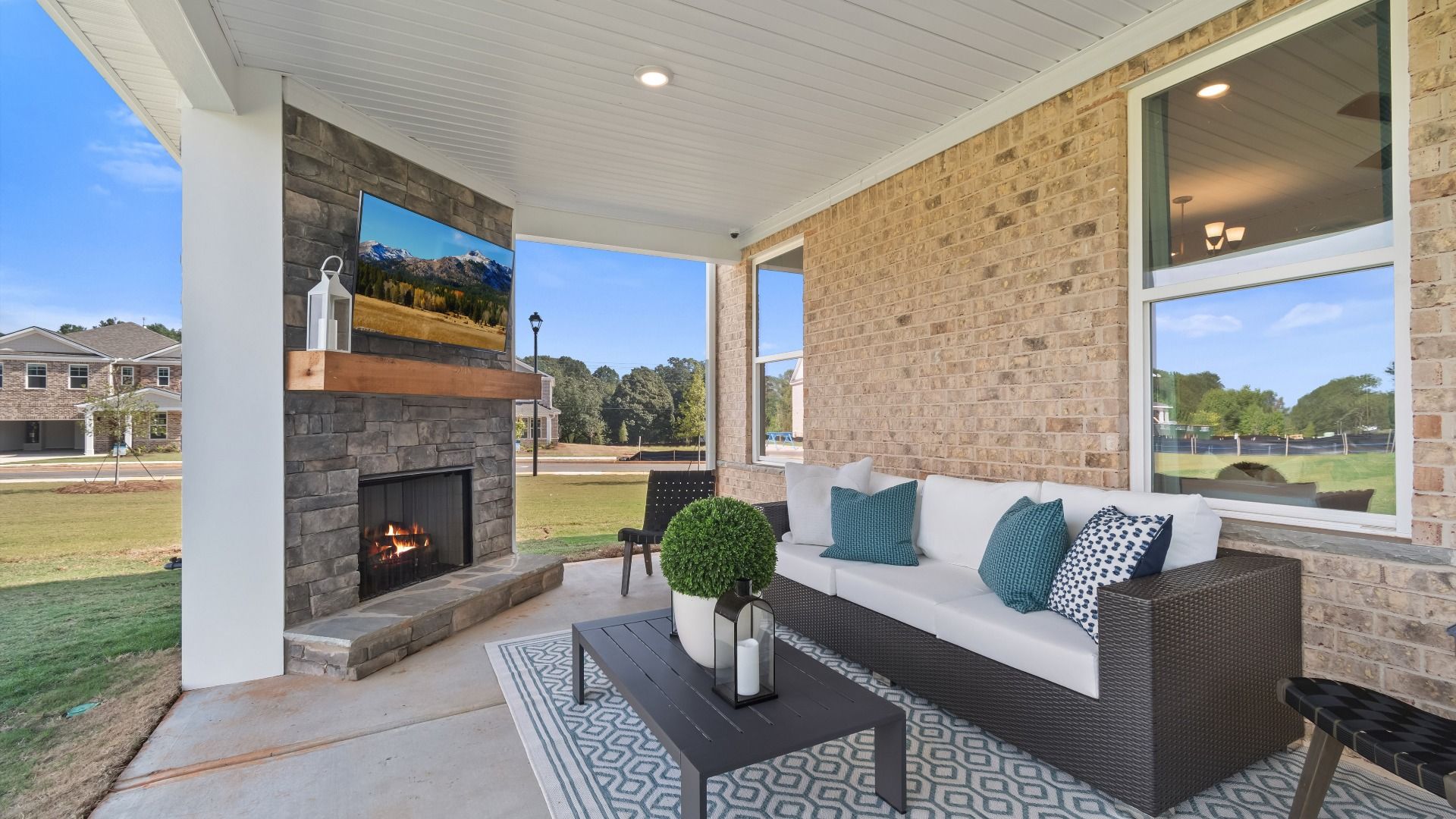 Covered gameday porch featuring corner stone fireplace, TV and spacious outdoor seating area in Burchwood in Stockbridge, GA.