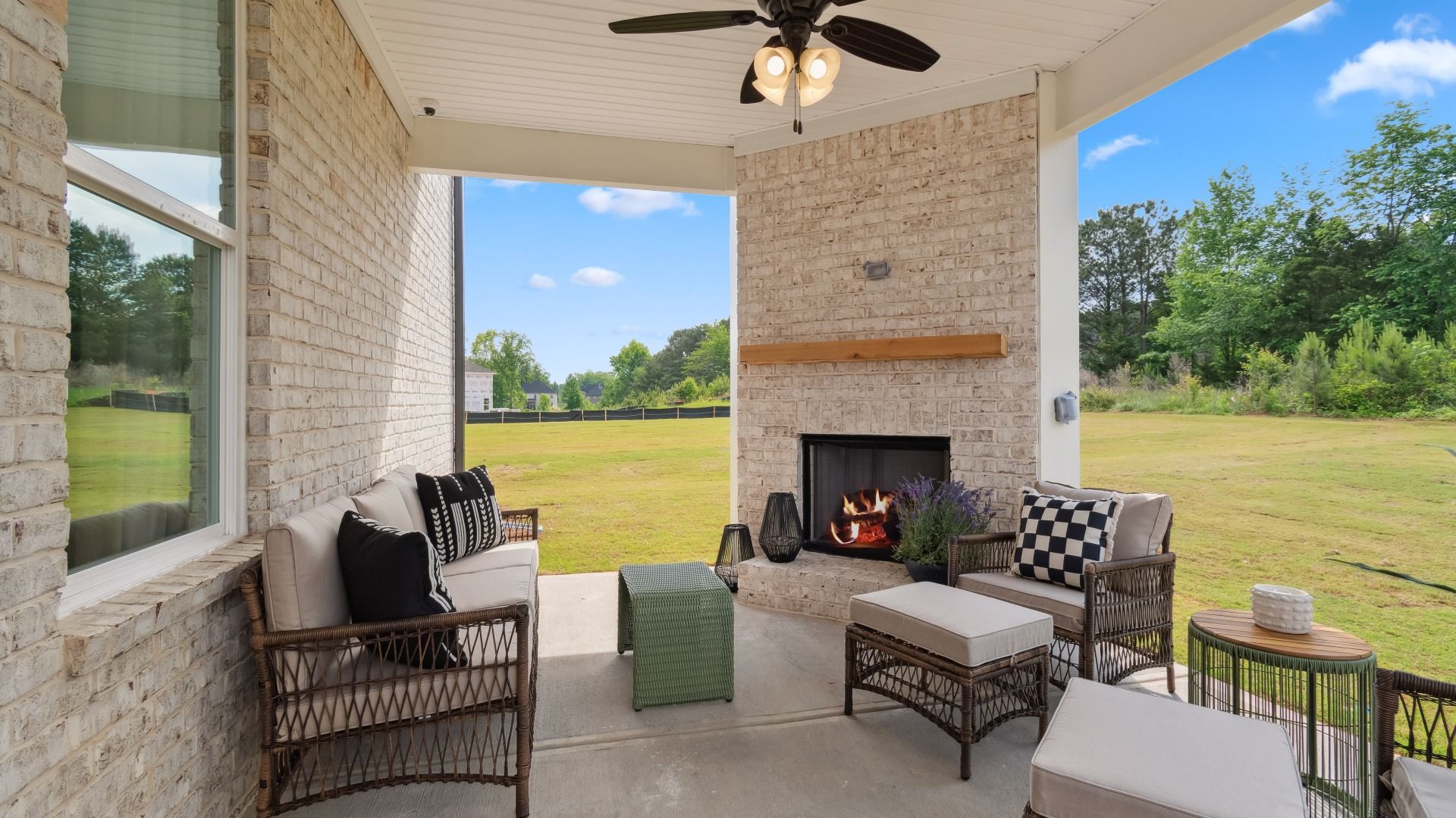 Covered gameday porch with brick gas fireplace, seating area, and views of open backyard at Westwind Estates in Hampton, GA.