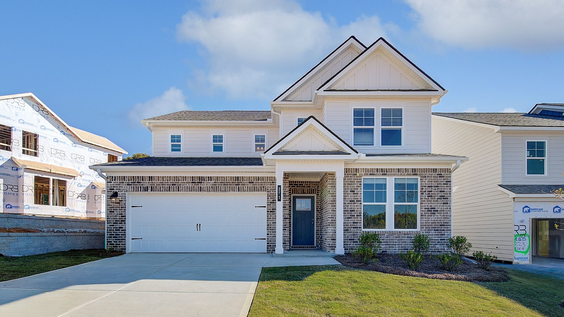 New construction home with dark gray trim and columns, warm white fiber cement accents, and brown brick at Abbotts Crossing.