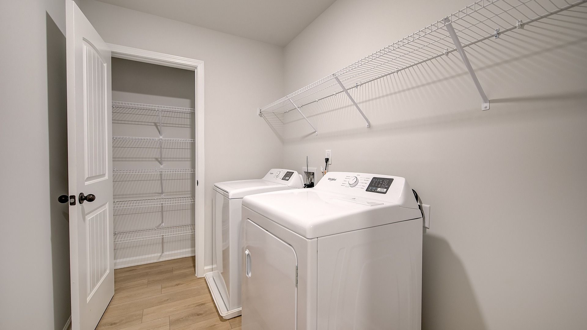 Laundry room with closet space, built-in shelves, and LVP flooring in the Mitchell at Avery Landing in McDonough, GA.