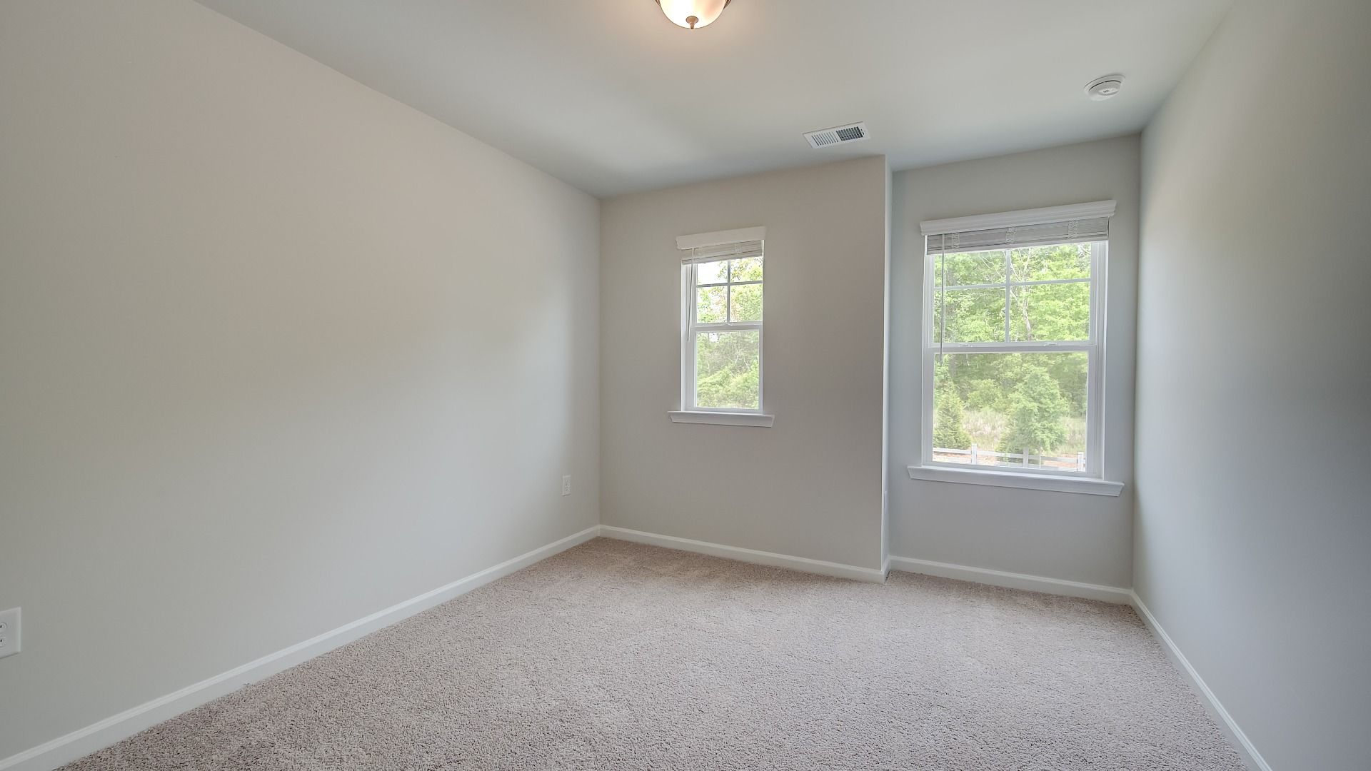 Secondary bedroom with abundant natural light and carpet flooring in the Mitchell new construction townhome.