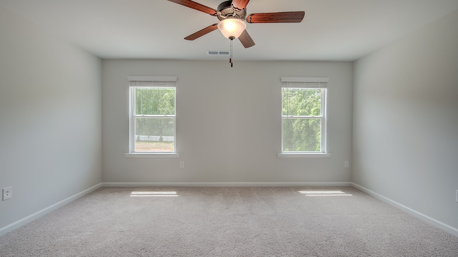Spacious primary suite with natural light, carpet flooring, and overhead fan light in the Mitchell at Avery Landing.