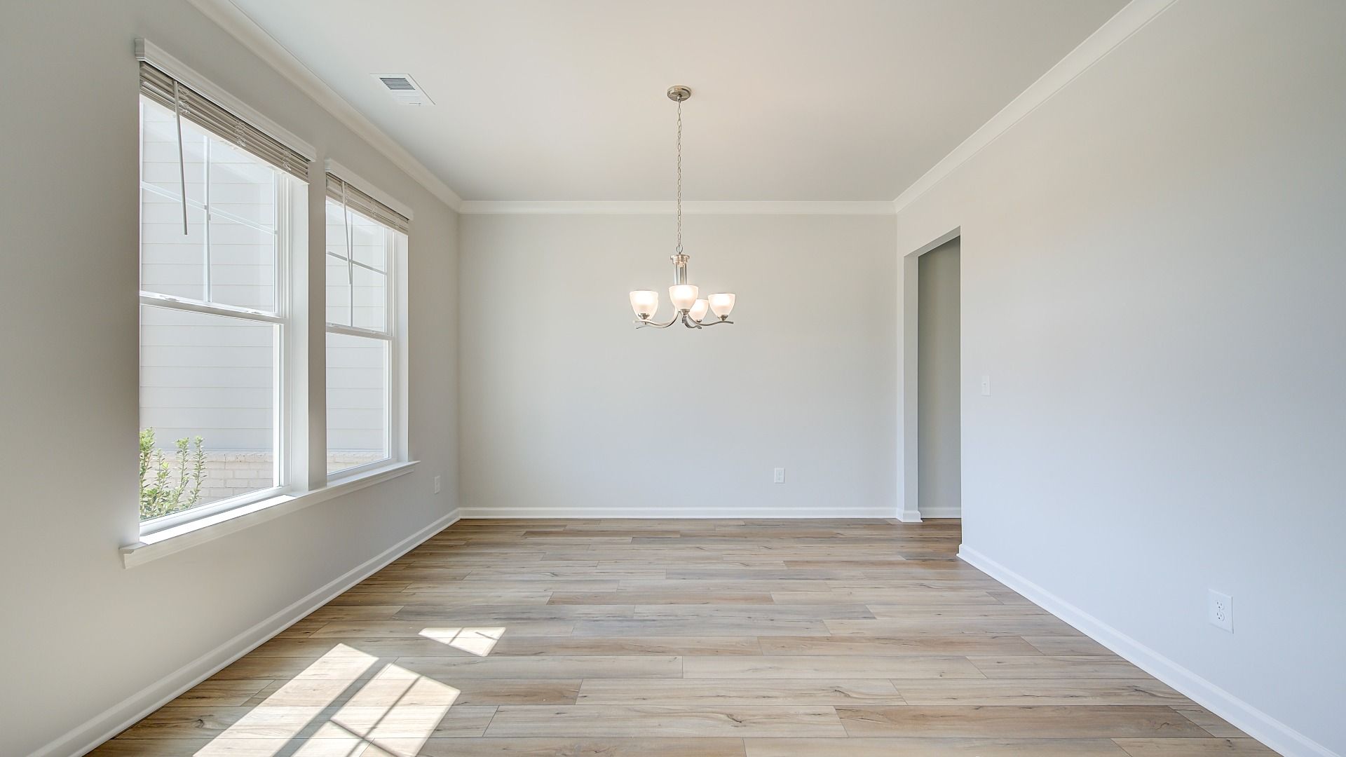Open dining room with chandelier lighting, large windows, and LVP flooring in the Clarity at Brighton in Locust Grove, GA.