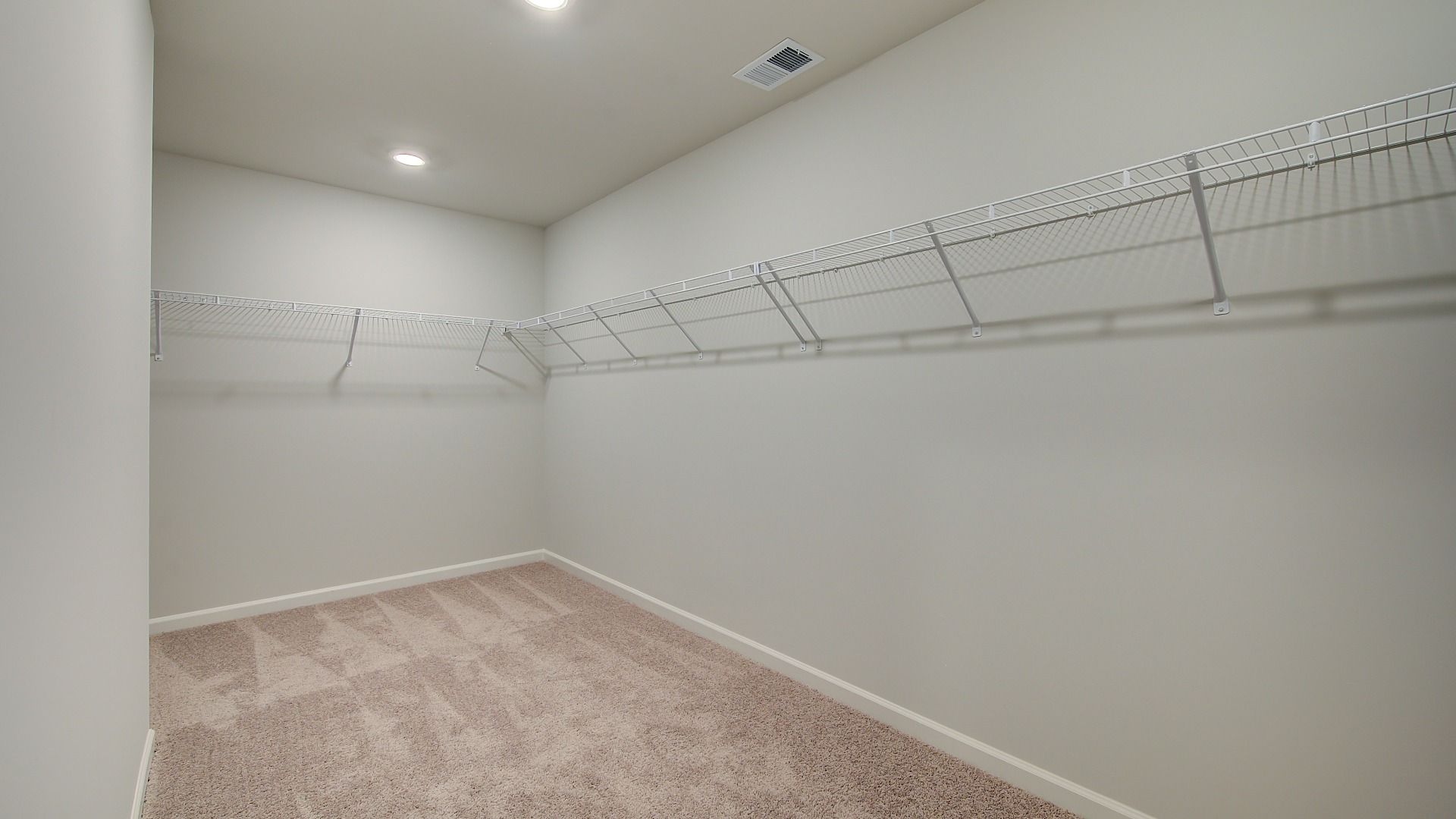 Primary closet connected to bath with carpet flooring and built-in shelving in the Clarity at Brighton in Locust Grove, GA.