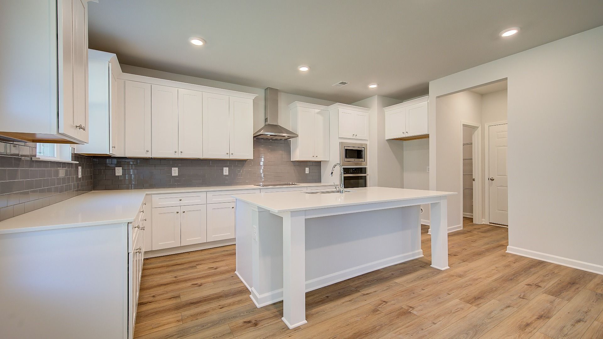 Open-concept Wagener kitchen with clean tile backsplash, white cabinetry, and large island with seating at Bowers Farm.